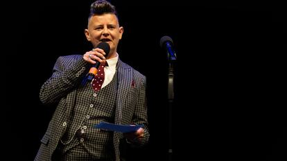 Joelle Taylor wears a checked three piece suit holding a microphone