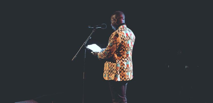 A poet stands at the microphone, performing at Out-Spoken