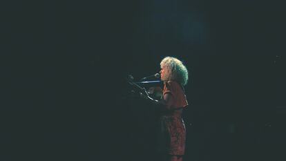 A woman stood on a dark stage, playing the guitar