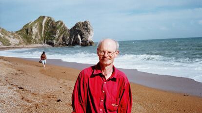 Poet Gavin Selerie wears a red shirt standing on the beach at Durdle Door