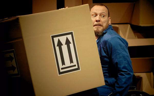 Person with a concerned expression holding a large cardboard box with two upwards arrows on it.