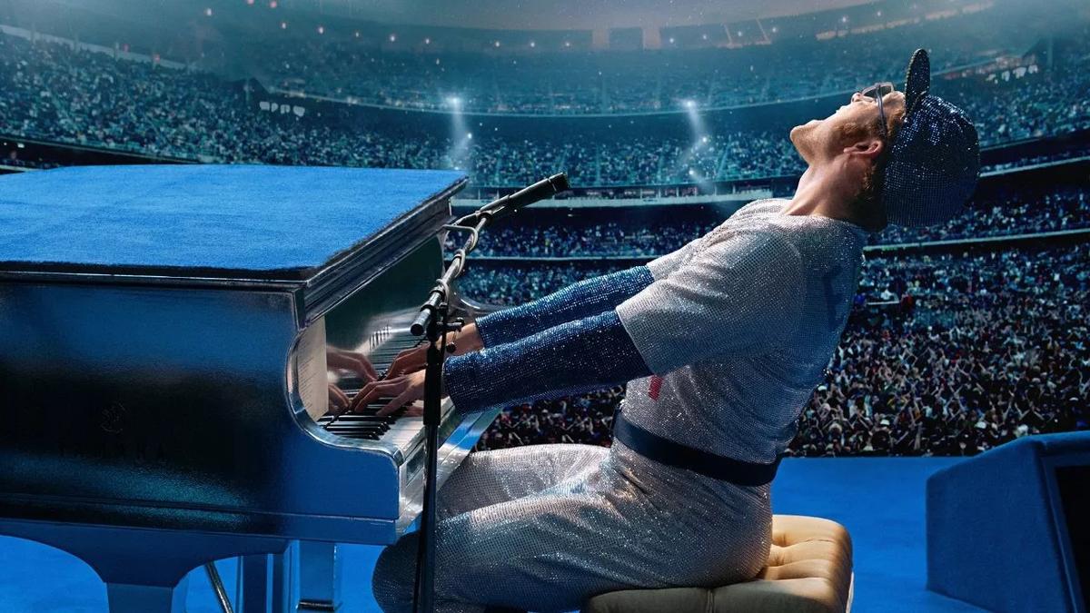 Yound Elton John (portrayed by Taron Egerton) plays piano in the old Wembley Stadium