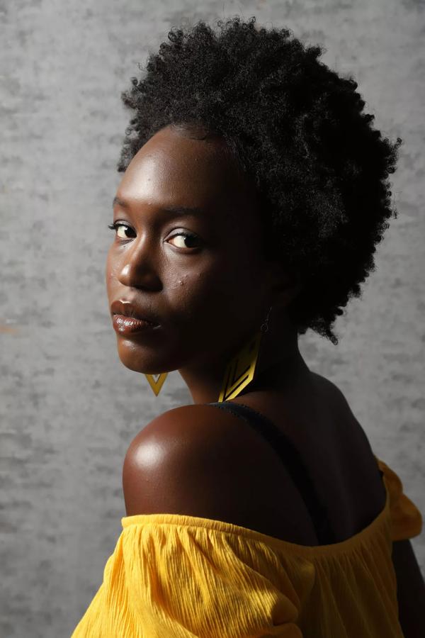 Artist Zamar looks over a shoulder wearing a yellow top and earrings