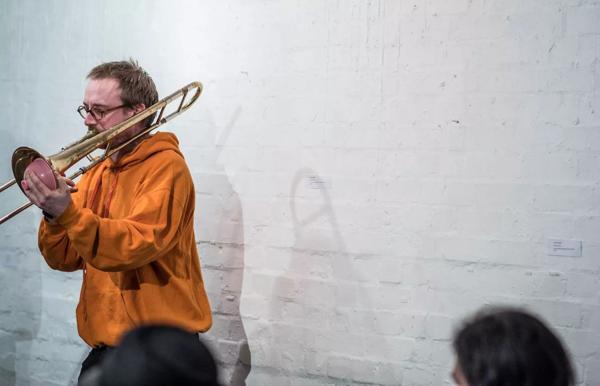 Alex Pacton plays the trombone in front of a whitewashed wall