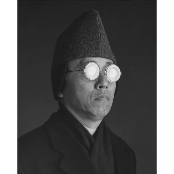 Black and white portrait of Hiroshi Sugimoto wearing a hat and reflective round glasses
