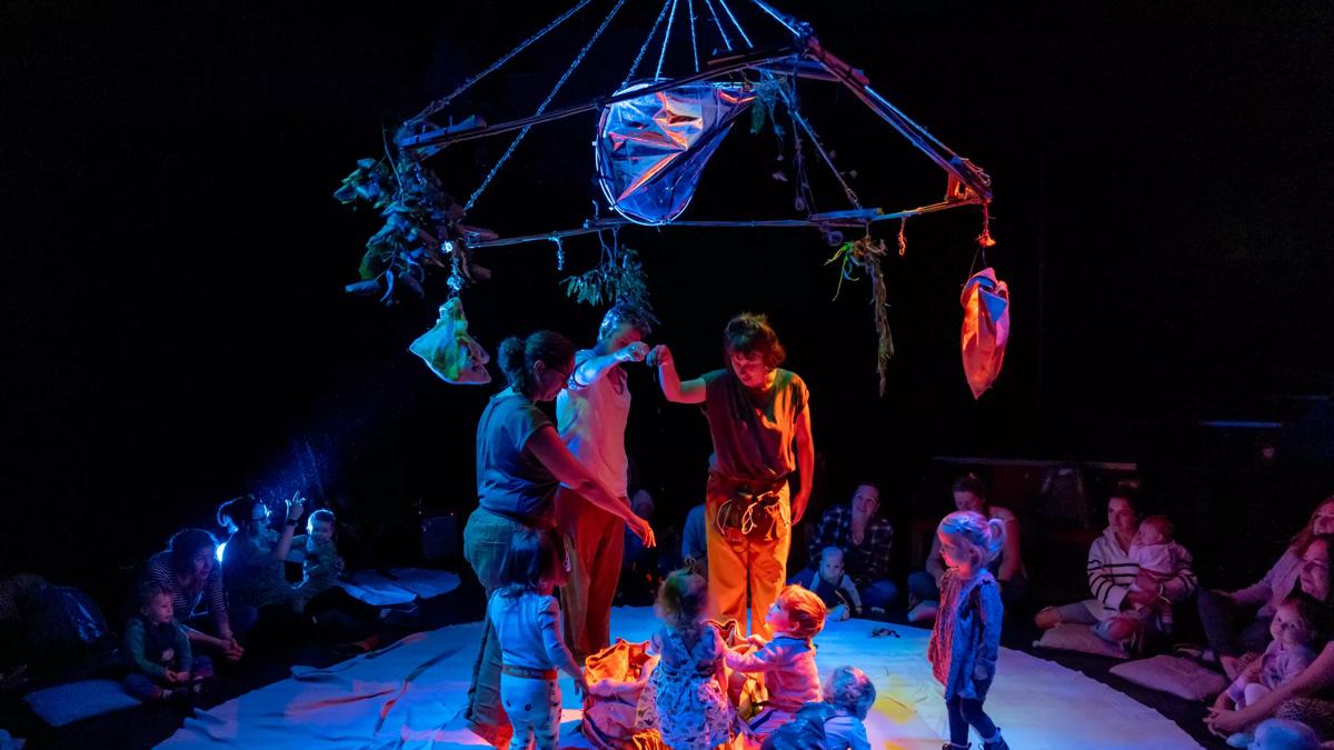 Performers and children stand in a circle with a bright box in the middle