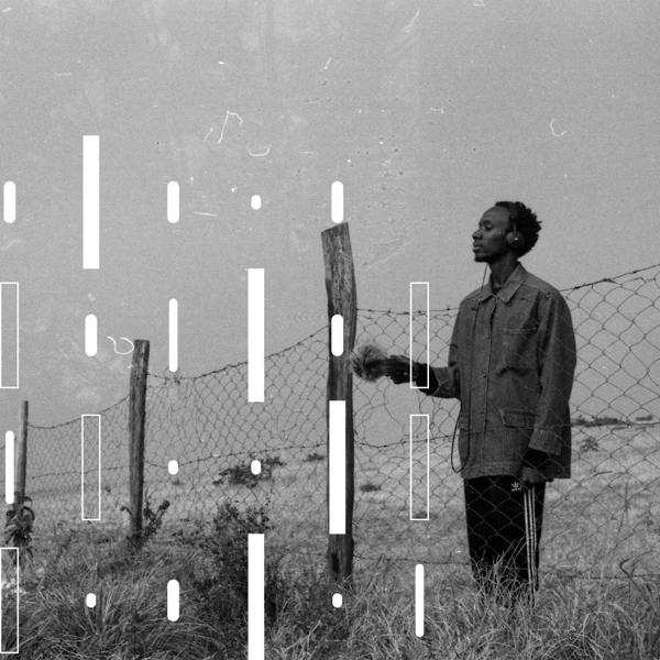 Artist KMRU standing on a field near a fence with headphones