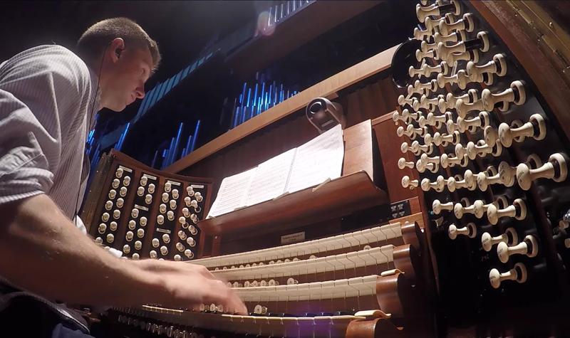 The Royal Festival Hall organ console, featuring a baffling number of white knobs; organist James McVinnie, a White man with a buzz cut is playing the organ keys