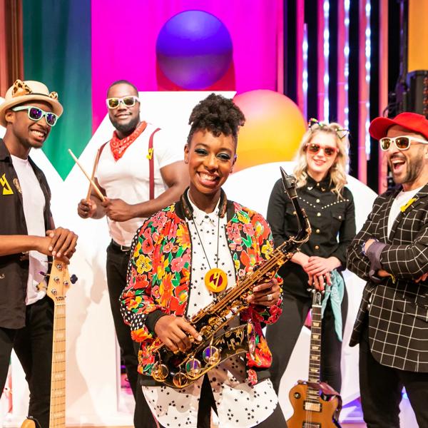 YolanDa Brown wearing a colourful jacket holding a saxophone surrounded by her band.