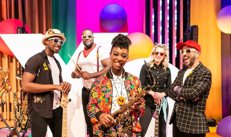 YolanDa Brown wearing a colourful jacket holding a saxophone surrounded by her band.
