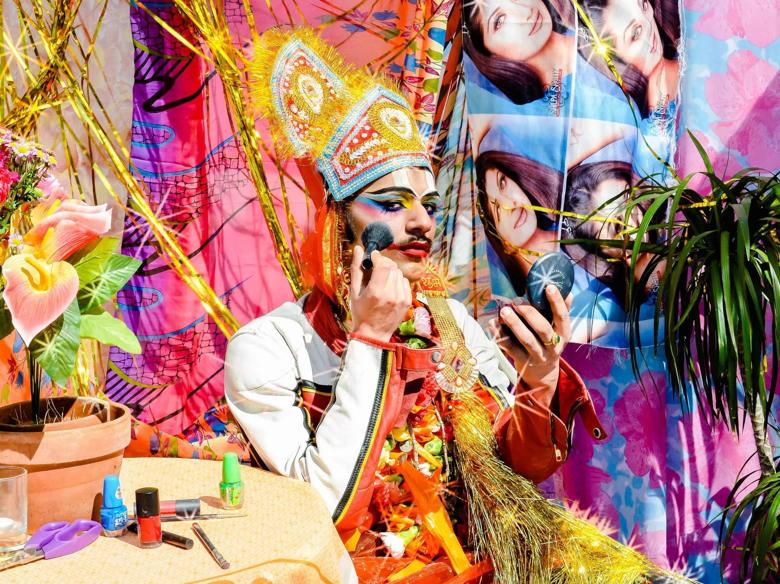 Nazar, person putting on makeup in a colourful background setting