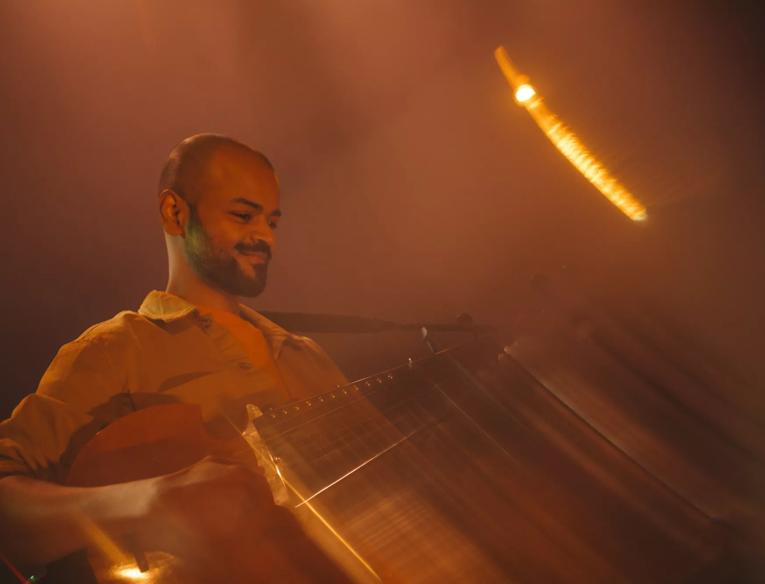 Soumik Datta playing an instrument with a blurry focus and orange lighting.