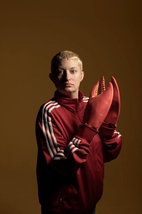 Comedian Harriet Dyer wears a red sports jacket with lobster claw gloves over her hands