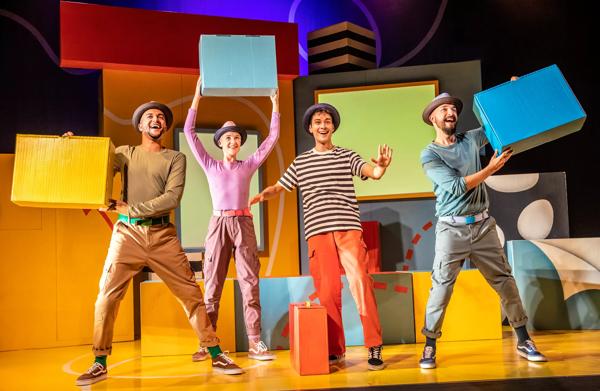 Four actors stand on stage holding up colourful boxes and wearing hats.