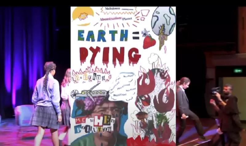 Children walking across a stage with a poster saying 'Earth = Dying'