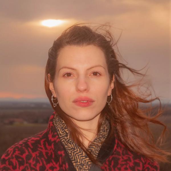 Artist Soap&Skin stands looking at the camera in a patterned red jacket with her hair blowing in the wind. 