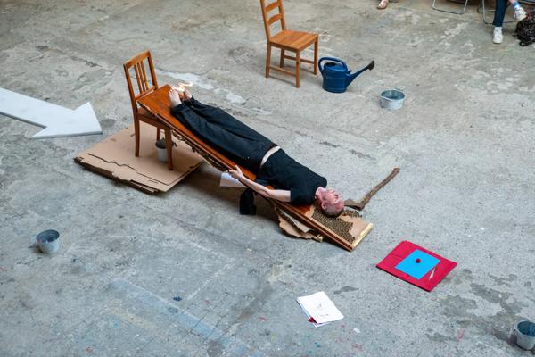 A man lying on his back on a wooden plank that is balanced on a wooden chair