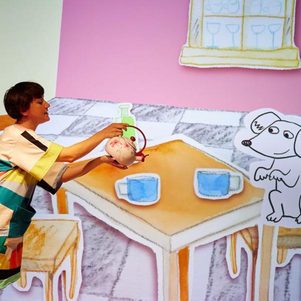 A person pours a teapot in front of a cartoon table setting.