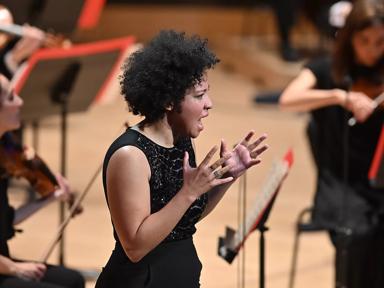 Singer Julia Bullock performing with the Philharmonia, hands outstretched and wearing a black sequinned sleeveless top