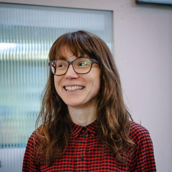 Author Ania Bas, smiling and wearing glasses in a portrait photograph by Ashley Carr