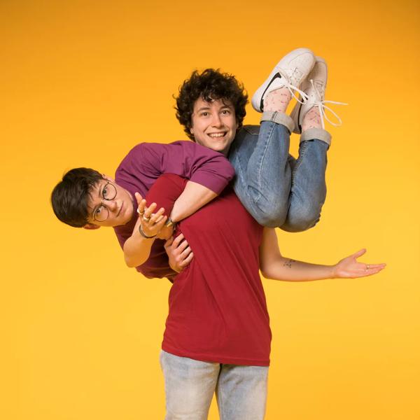 Person balancing on someone's shoulders against a yellow background. 