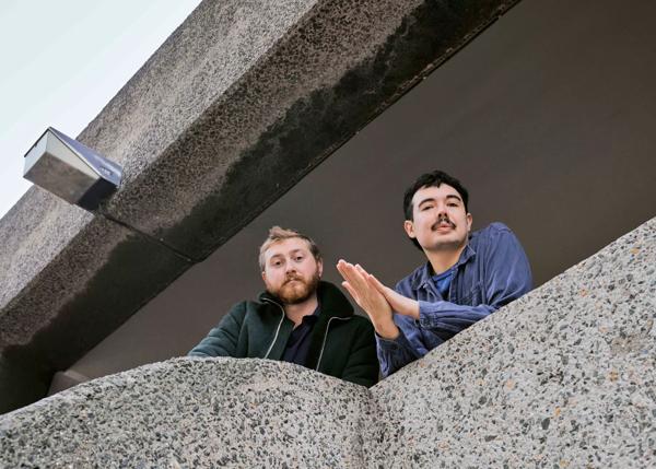 The Deptford Northern Soul Club duo, Will Foot and Lewis Henderson, lean over the stone balcony of a building.