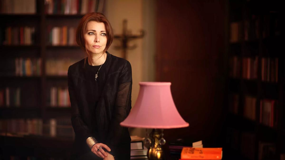 Elif Shafak standing in a library next to a pink lamp
