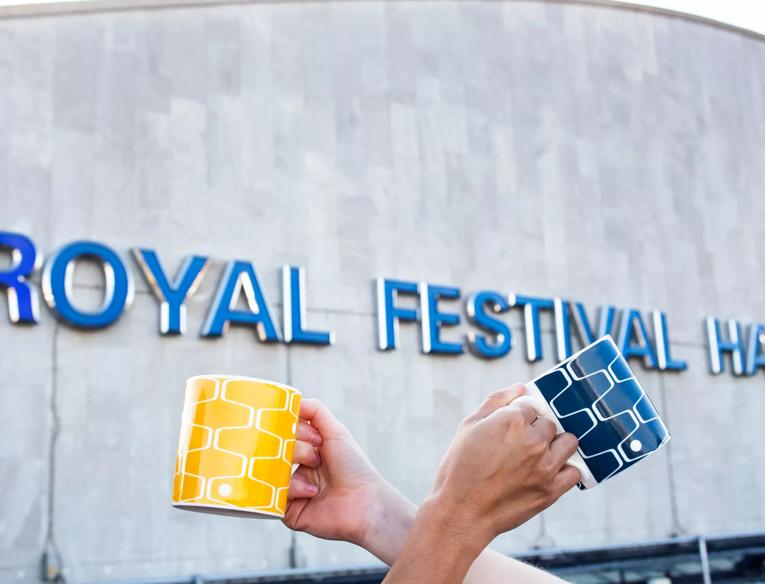 Two Net & Ball mugs held in front of Royal Festival Hall signage