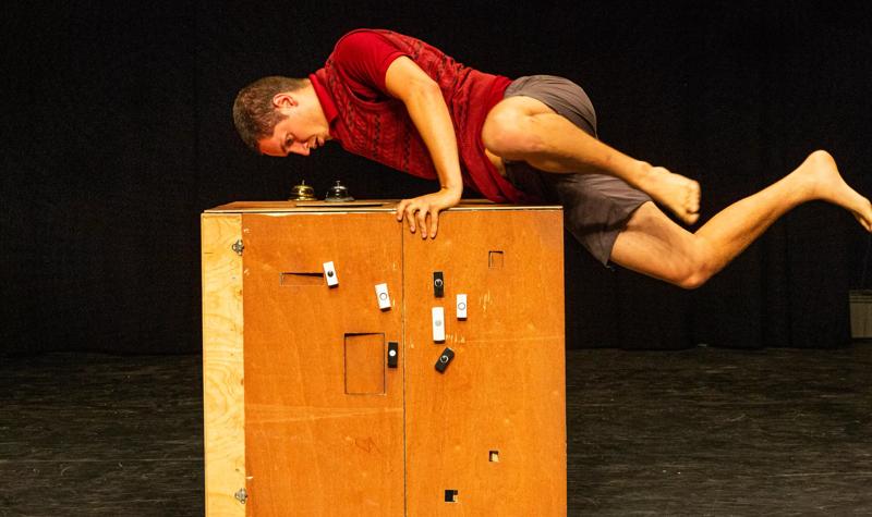 A performer balances on his bands on a wooden box.