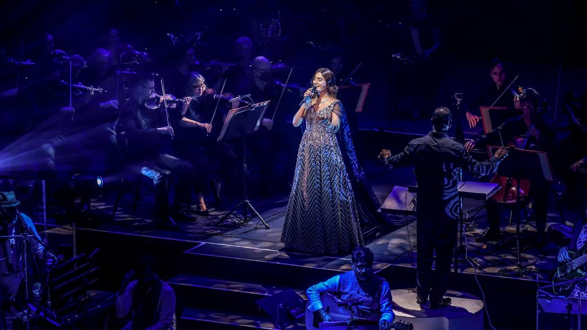 Person with a blue sparkly dress singing on stage with an orchestra 