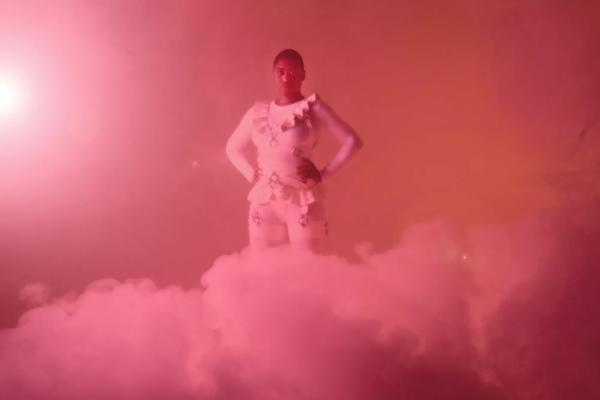 Person standing in a pink cloud wearing white bondage gear.