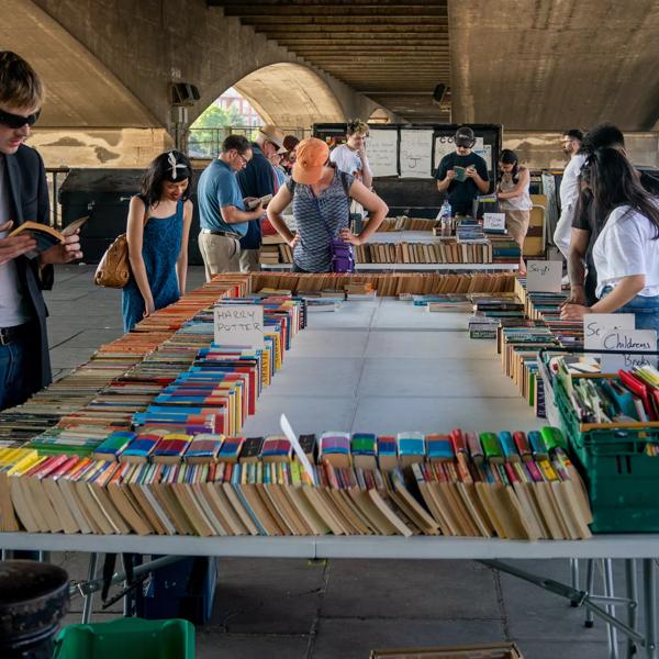 Several people look at the books on offer on a large table, part of the South Bank Book Market