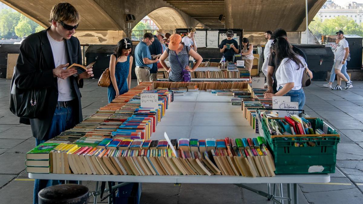 Several people look at the books on offer on a large table, part of the South Bank Book Market