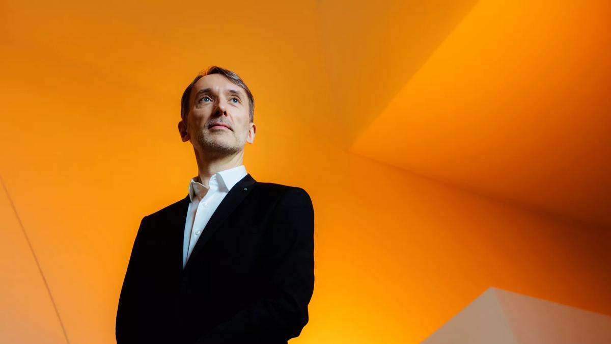 Organist Olivier Latry in a black suit in an orange room