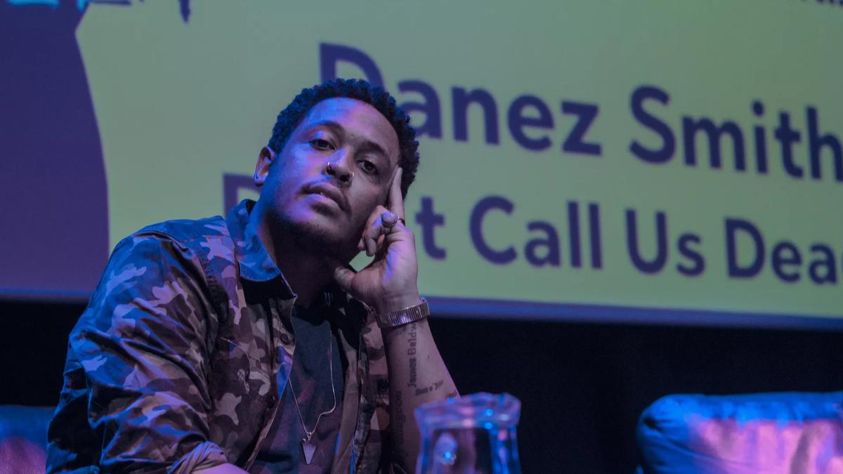 Danez Smith sits onstage, wearing a camo jacket. 