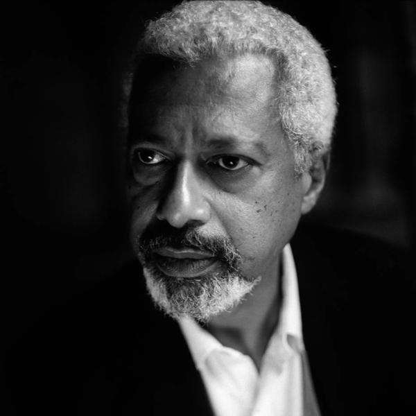 Black and white portrait of Abdulrazak Gurnah. He looks to the left of the camera and wears a white collared shirt.