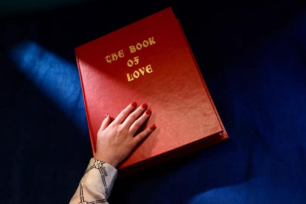 Hand resting on a red leather bound book with the title 'The Book of Love'.
