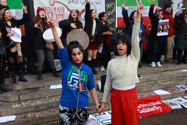 Two women stand holding hands and raising peace symbols at a protest.
