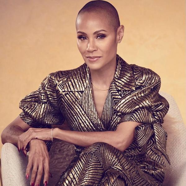 Jada Pinkett Smith is sat on a beige armchair in a black and gold shiny suit