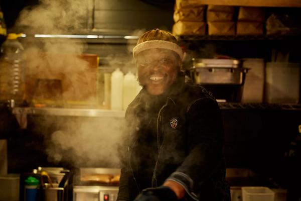 Photo of a trader at the Oh My Dog stand smiling whilst cooking hot dogs