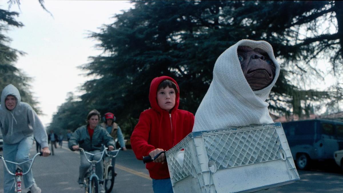 A boy wearing a red hoodie on a bike with an alien in a basket