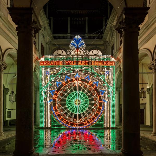 Marienella Senatore's work We Rise by Lifting Others. Neon lights sculpture with southern Italian illuminated decorations