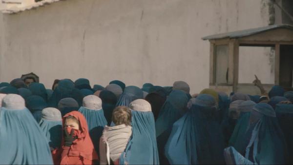 A crowd of women in blue burqas with one woman wearing a red veil