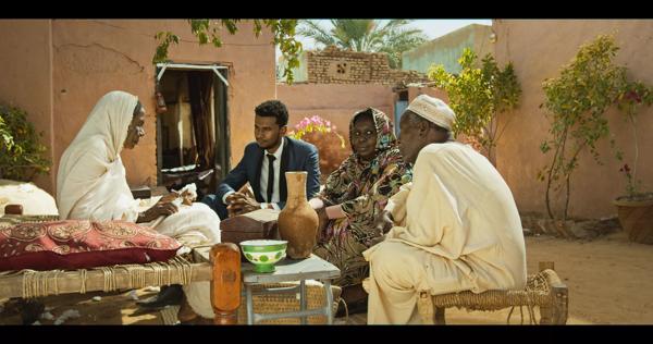 A group of Sudanese people sit conversing in a courtyard. 