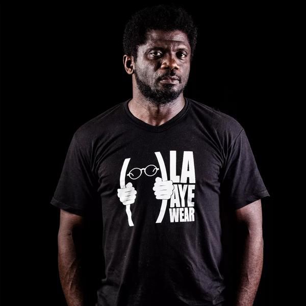GauZ’, a black man with short dark hair wears a black t-shirt and stands against a black background