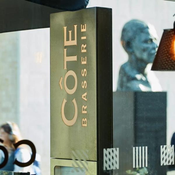 Cote Brasserie interior with logo in focus and Mandela statue in the background