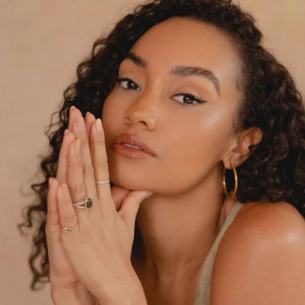 Leigh-Anne has her hands pressed together in a prayer position and resting to the side of her face. She has long curly dark hair and brown eyes and wears a camel coloured vest top. 