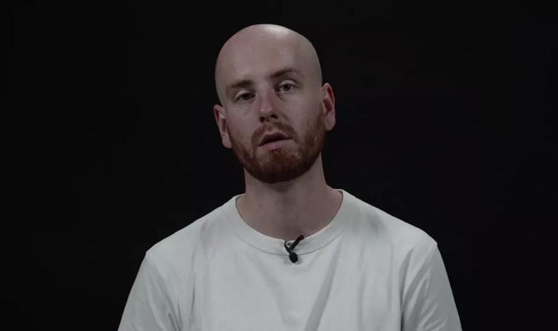 Joe Carrick-Varty, a young White man with shaved head and red stubble, wearing a white t-shirt reads from their TS Eliot Prize shortlisted collection against a black background