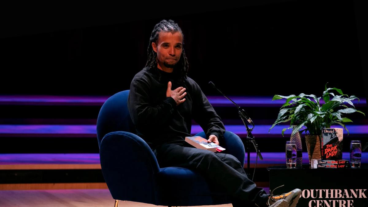 Akala sitting in a chair on stage