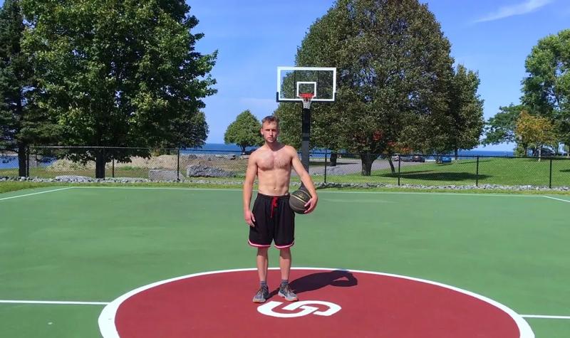 A shirtless man stands on an open air basketball court with a basketball under his arm; Cover image for the single 'Science Fair' by Black Country, New Road 